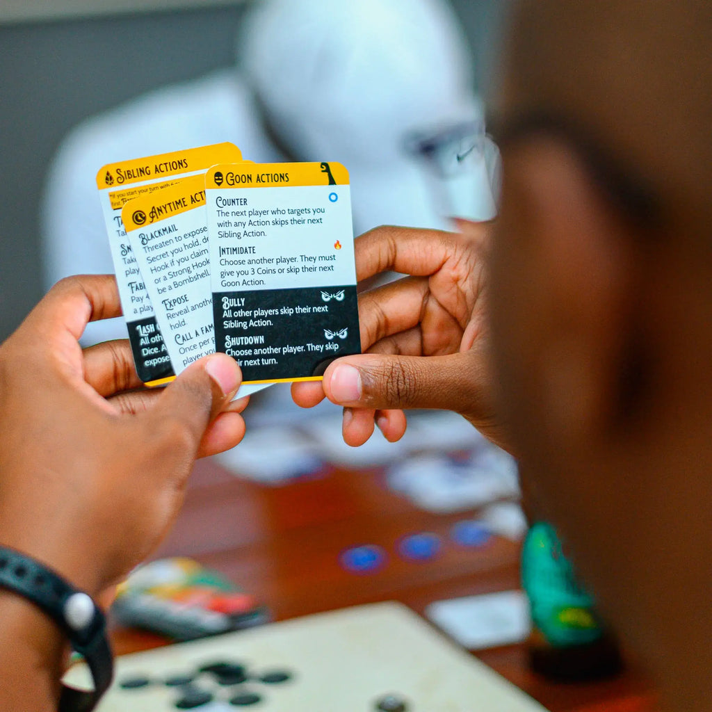 Two hands holding the three Action cards for the card game Thicker Than Blood on a blurred background