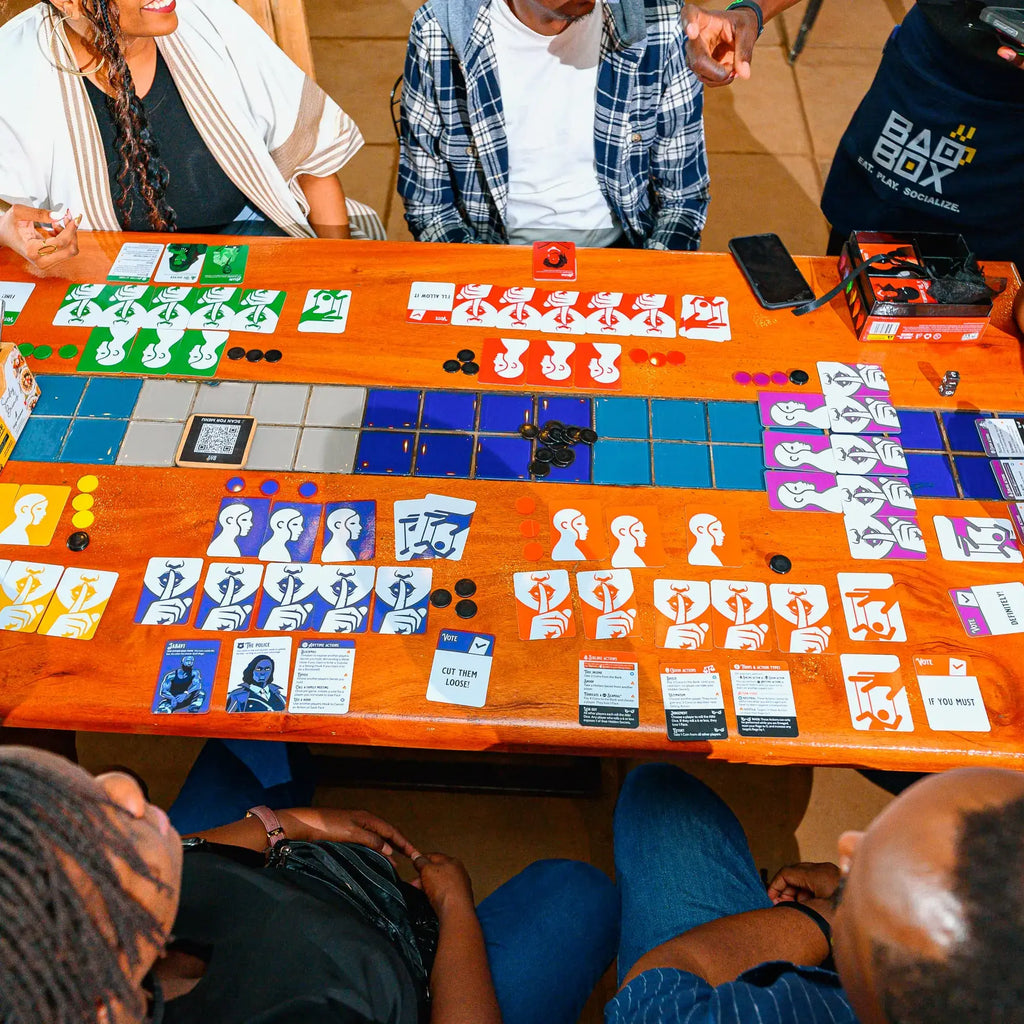 People playing a the card game, Thicker Than Blood with the colourful game token and cards setup and displayed on an wooden table.